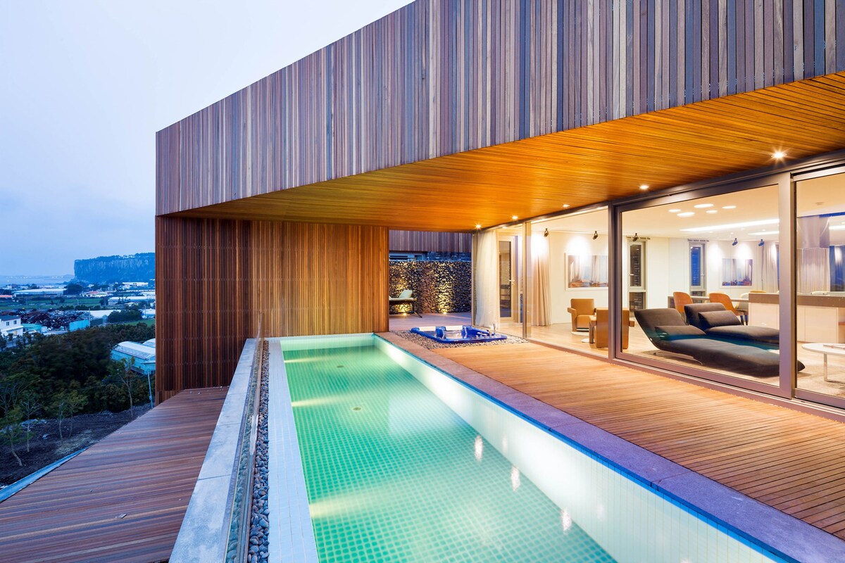 A modern building with a swimming pool, wooden deck, and a view of the landscape.