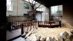 A covered outdoor area with a wooden deck, a small wooden structure, and a sandy ground. - Hotel Cullinan Yongin (Yongin)