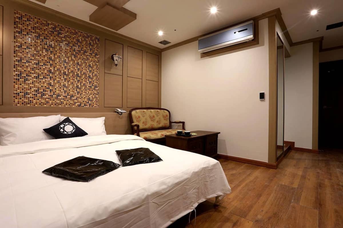 Une chambre d’hôtel avec un grand lit, une chaise, un bureau et un appareil de climatisation.
