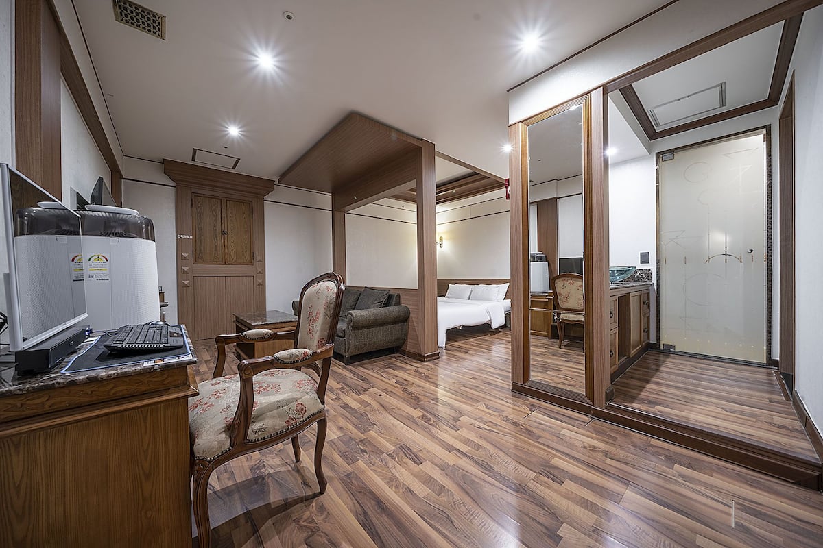 Une pièce spacieuse avec un plancher en bois, un bureau avec un ordinateur, une chaise, un lit et une armoire.