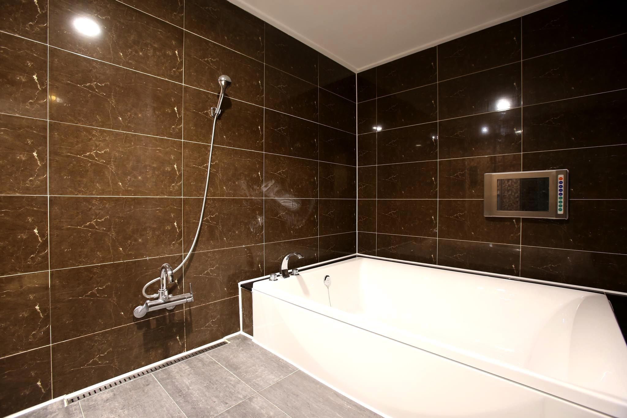 Un baño moderno con una bañera grande, un cabezal de ducha de mano y un panel de control en la pared.
