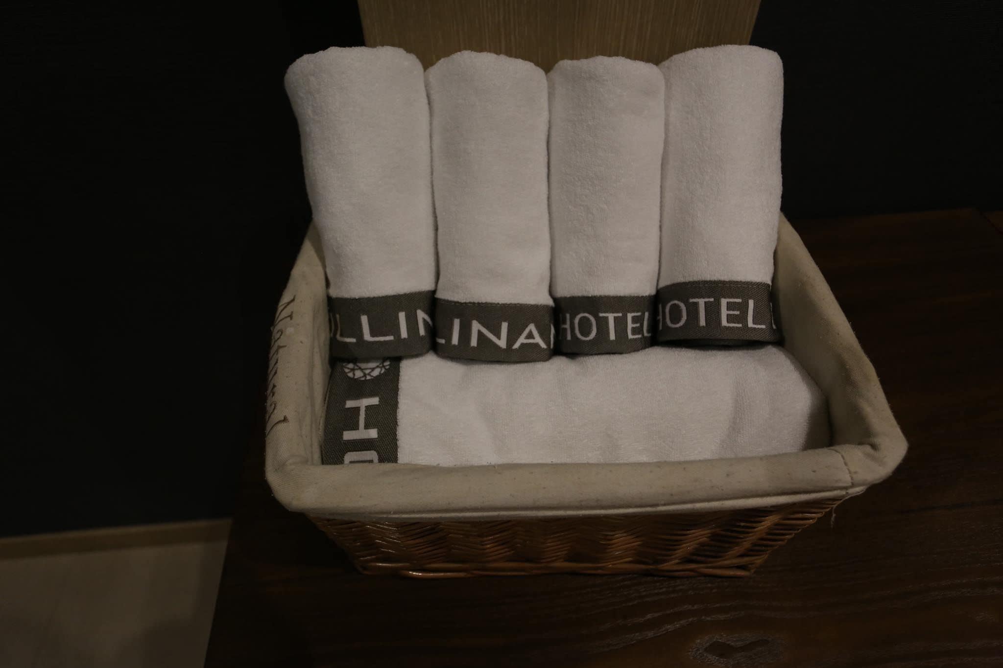 Un panier en osier contenant des serviettes blanches soigneusement pliées, avec une étiquette indiquant « HÔTEL LILINA ».