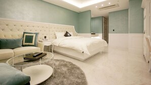 A modern bedroom with a tufted headboard, a round glass coffee table, a fluffy rug, and a large bed with white bedding. - Hotel Cullinan Yongin (Yongin)