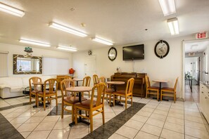 A dining area with wooden chairs and tables, a piano, a television, and an exit sign.