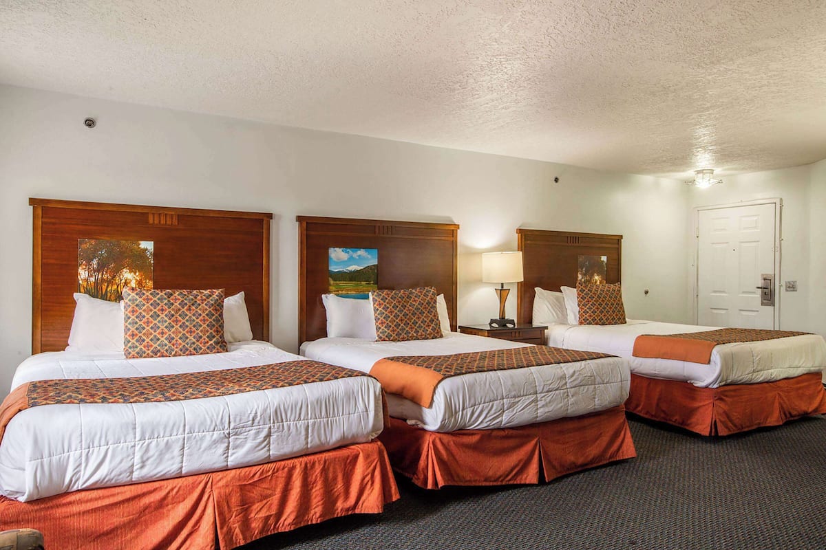 A hotel room with three single beds, each with a wooden headboard, white bedding, and orange accents.