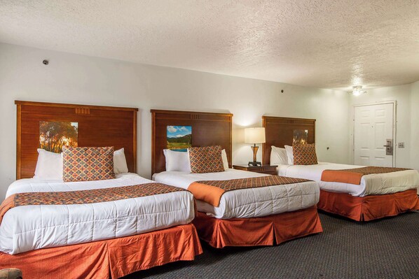 A hotel room with three single beds, each with a wooden headboard, white bedding, and orange accents.