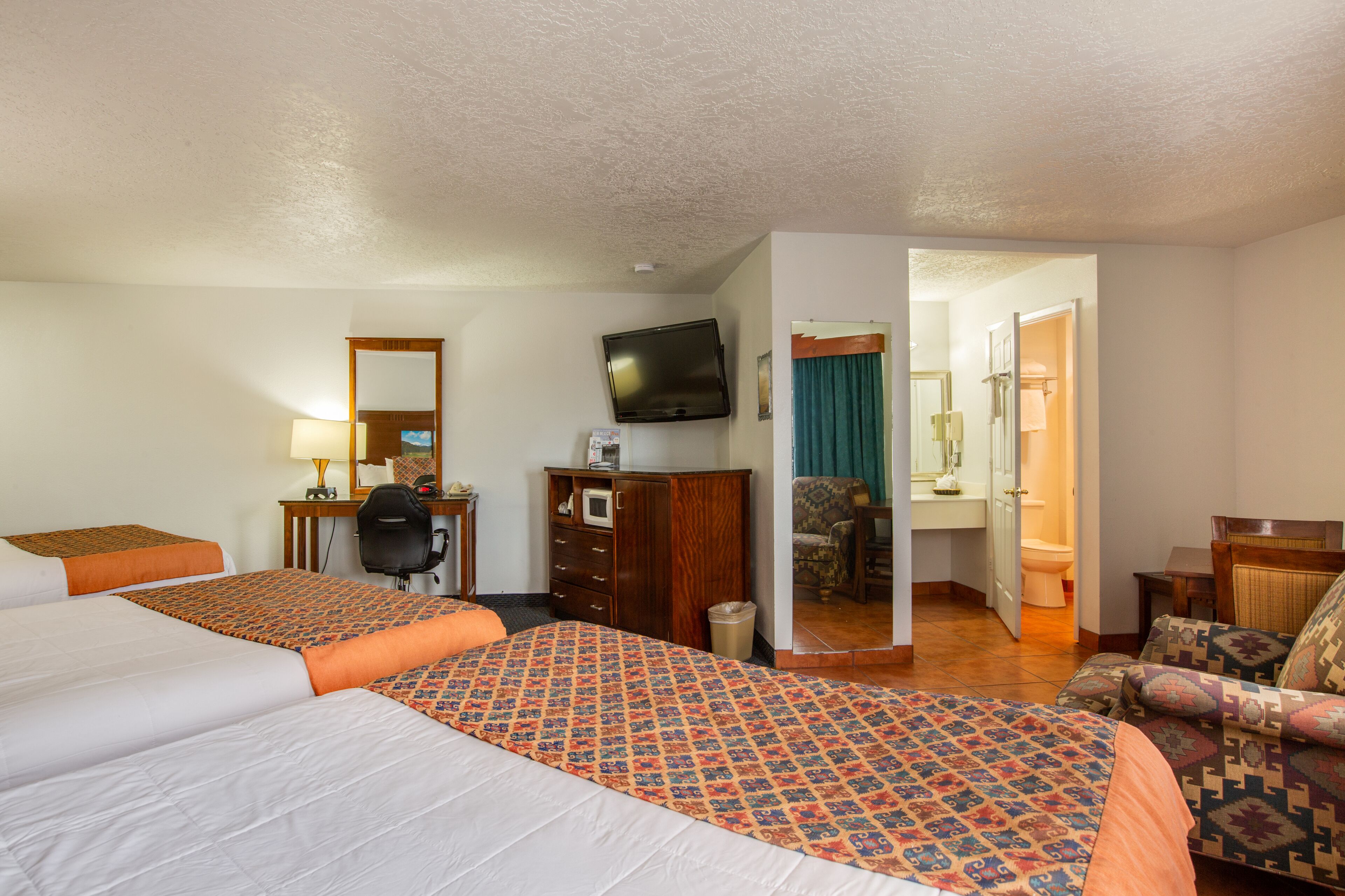 A hotel room with two beds, a desk with a chair, a television, and a bathroom visible through an open door.