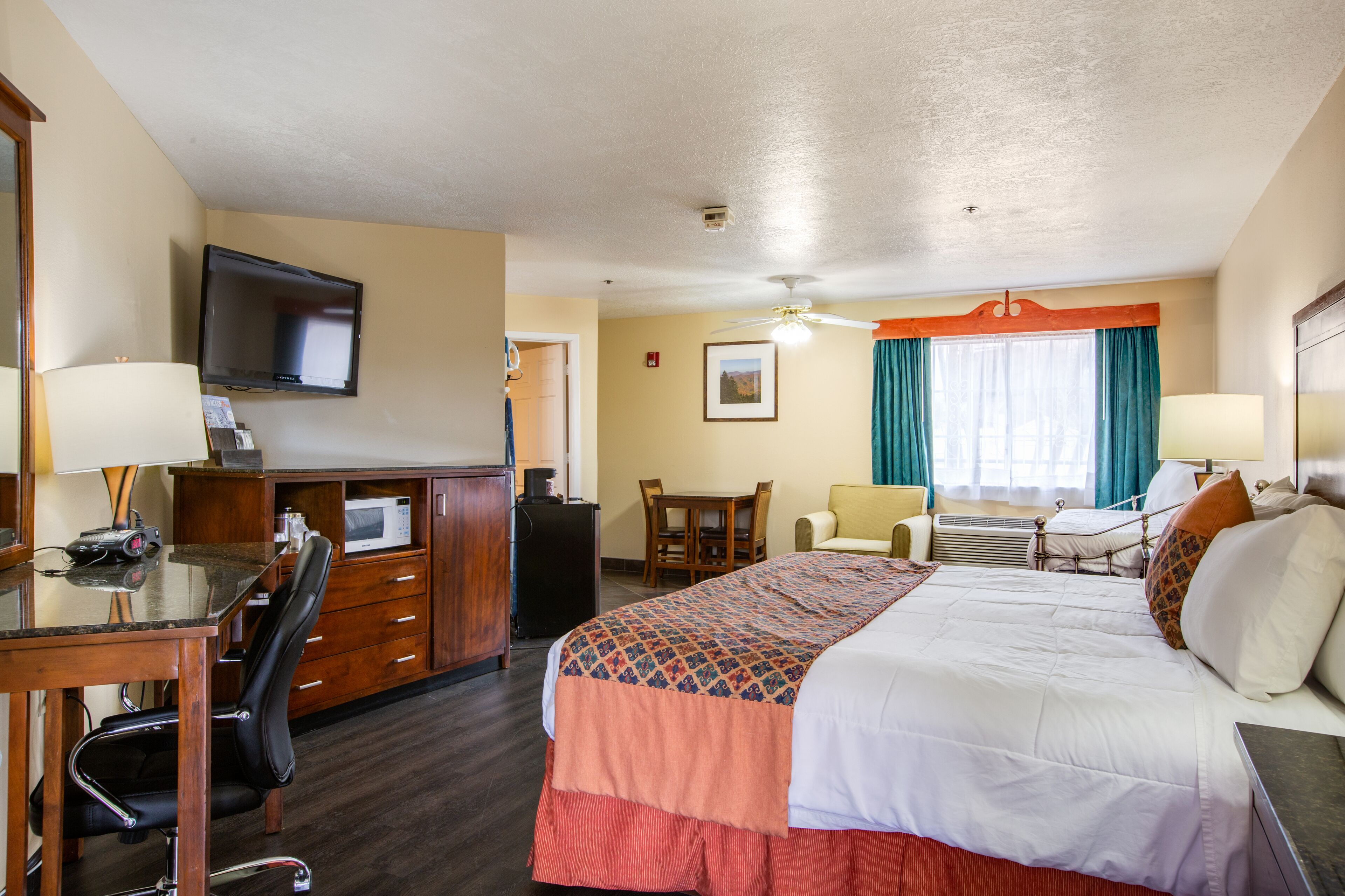 A hotel room with a bed, desk, chair, television, and a small table.