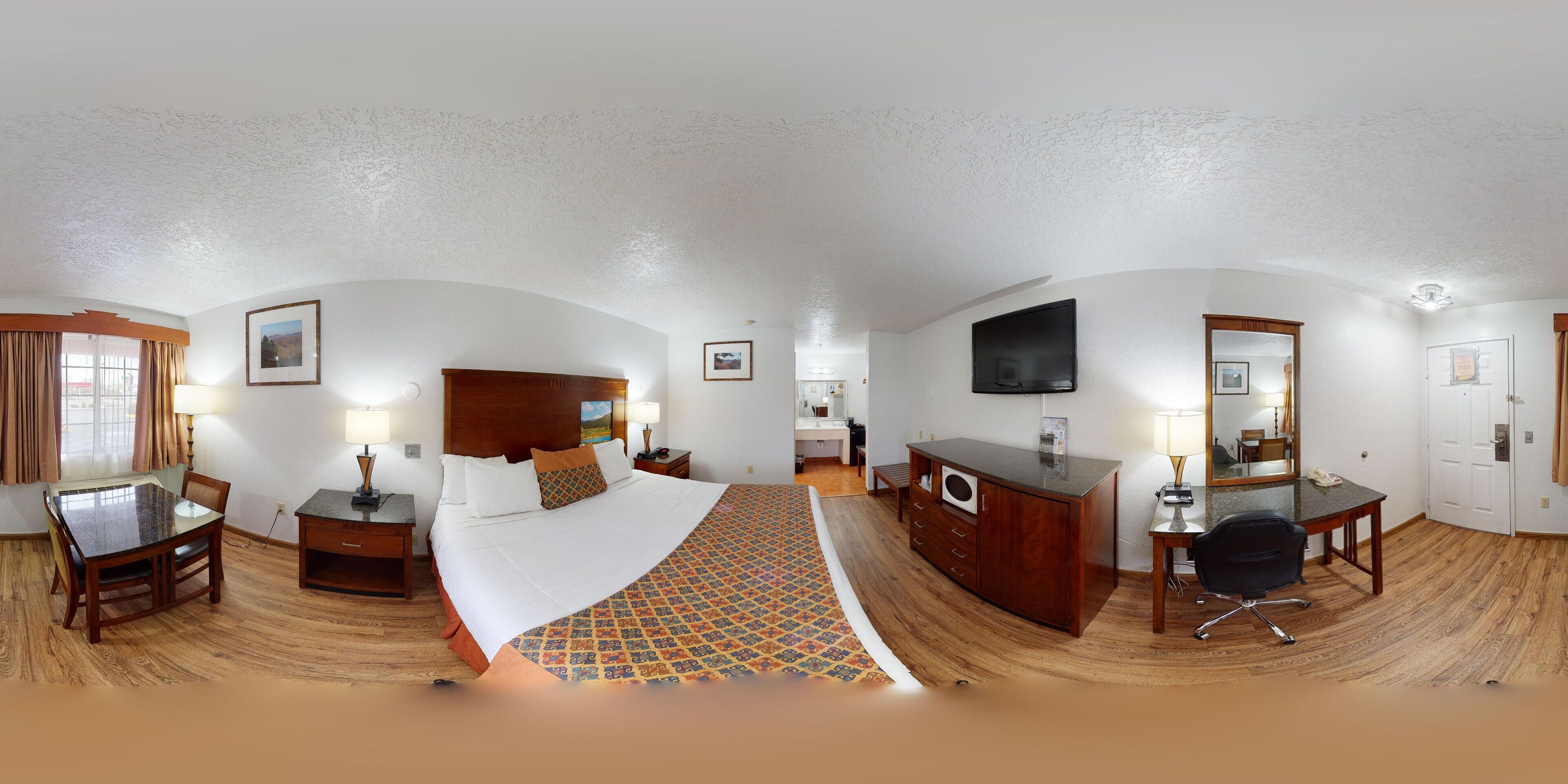 Habitación de hotel con cama, escritorio, cómoda, televisor y baño.