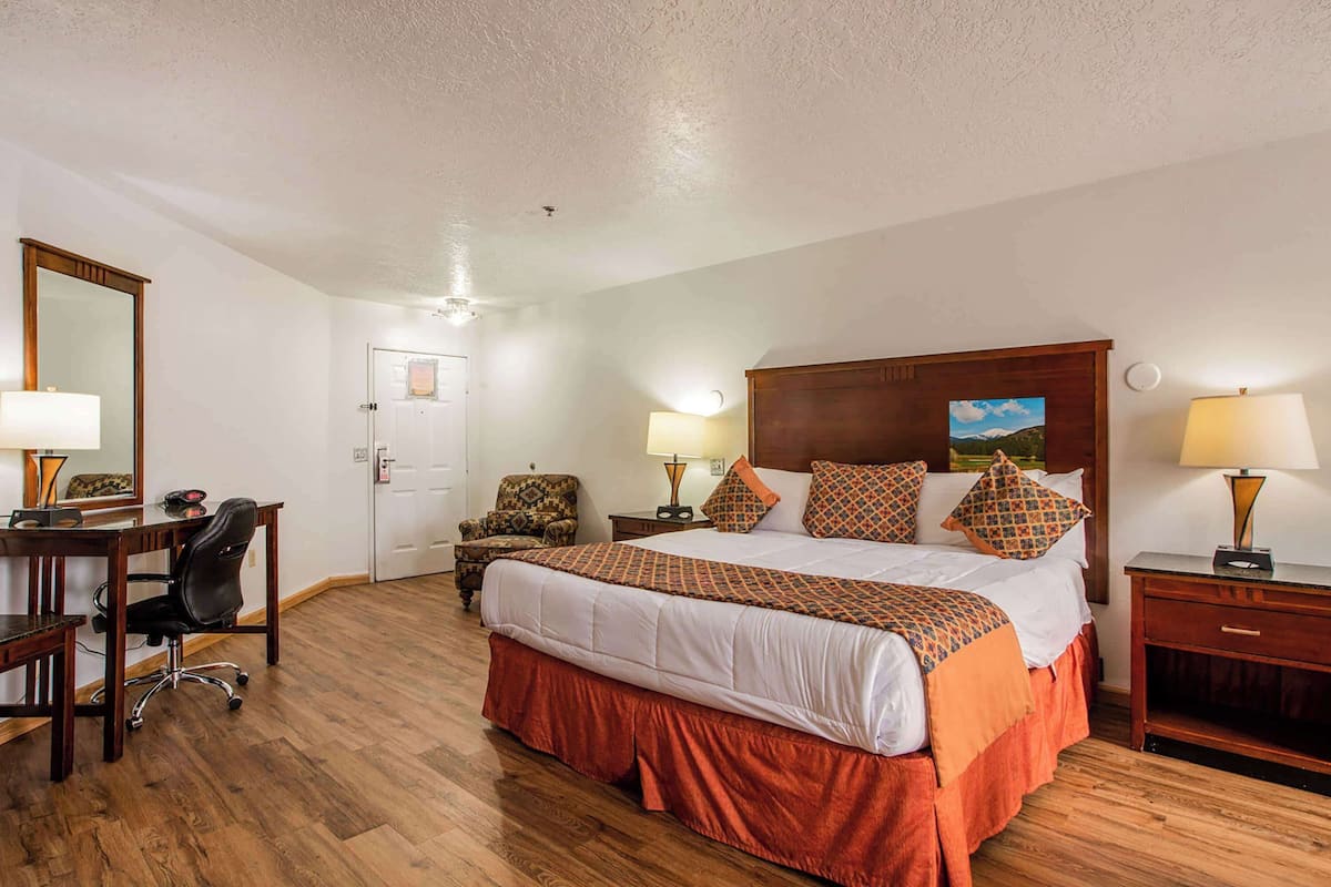 A hotel room with a large bed, a desk, a chair, a nightstand, and a lamp.