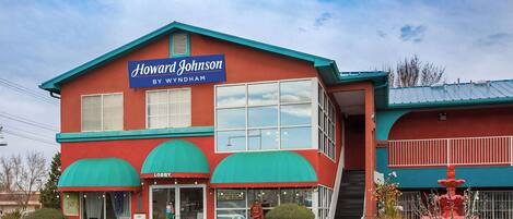 Un edificio de dos plantas con fachada roja y toldos verdes, identificado como "Howard Johnson By Wyndham".
