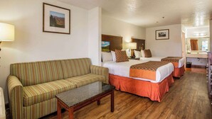 A hotel room with a striped sofa, two single beds, a small table, and a wooden floor. - Sandia Peak Inn Old Town ABQ, a Howard Johnson by Wyndham (Albuquerque)