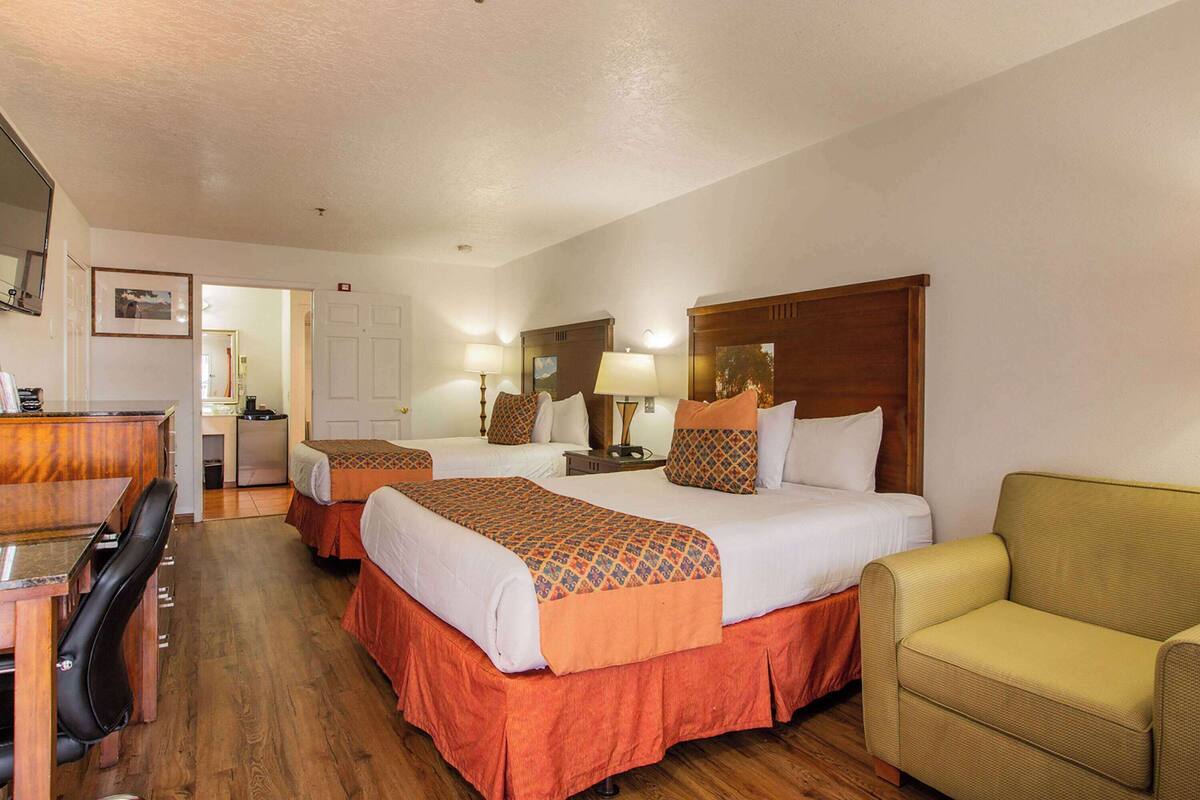 A hotel room with two beds, a desk, a chair, and a sofa.