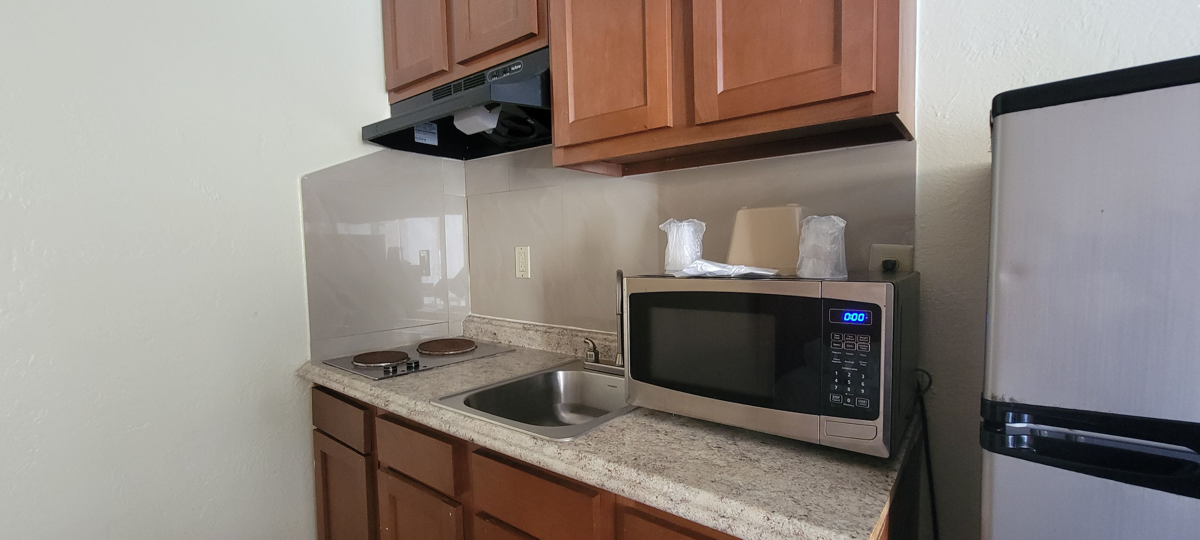 A compact kitchen with a stainless steel microwave, a built-in oven, and a refrigerator.