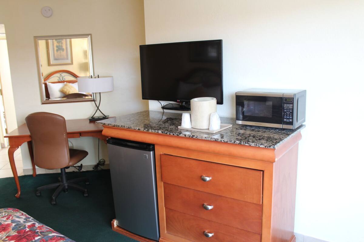 Ett hotellrum med ett skrivbord, en tv, en mikrovågsugn, ett kylskåp och en stol.