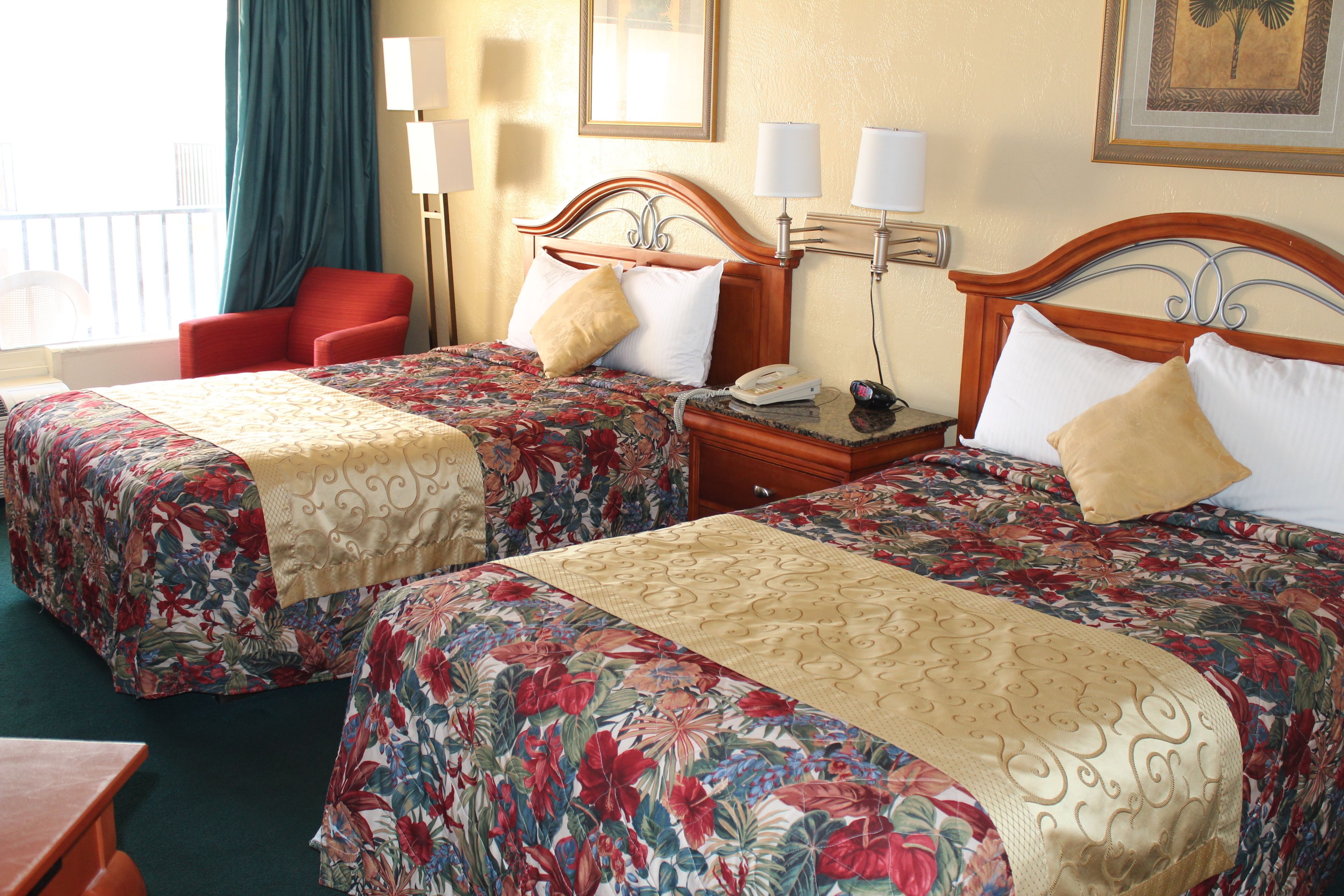 Habitación de hotel con dos camas, una silla, una mesita de noche y un ventanal con cortinas.