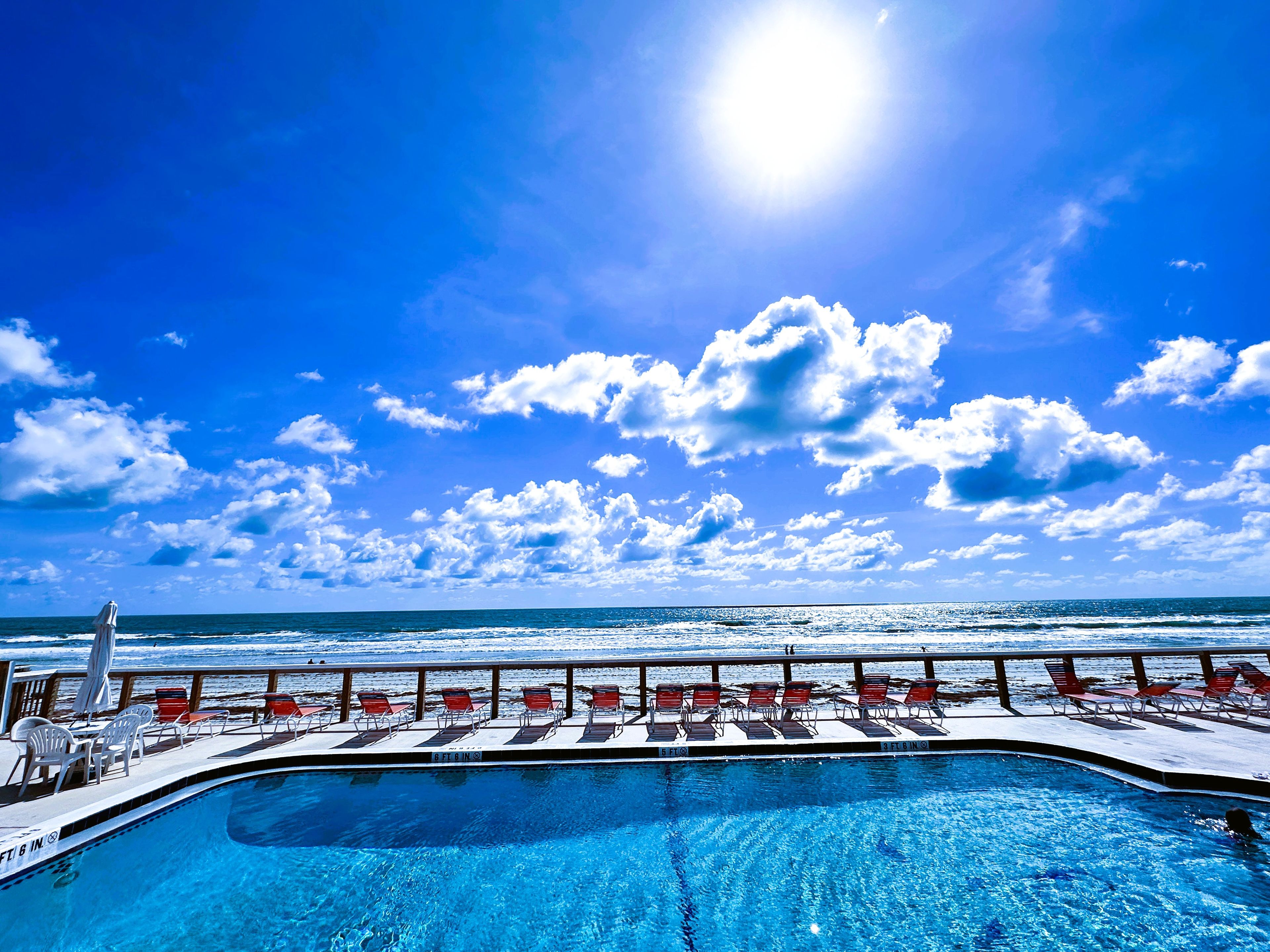 Zona de piscina con vista al océano, sillas de descanso y cielo despejado.