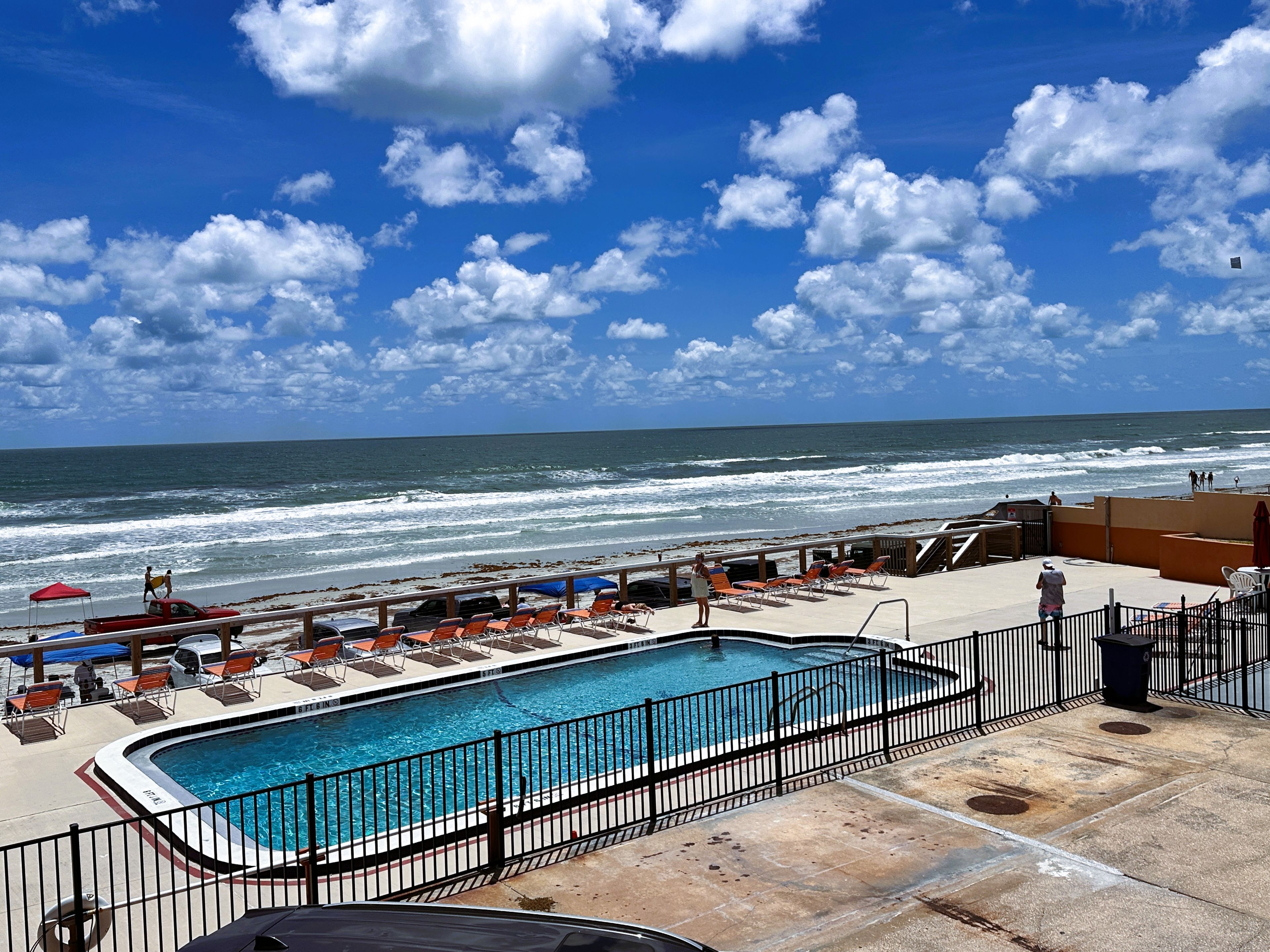 A pool area with a view of the ocean, a fenced pool, and beach chairs.