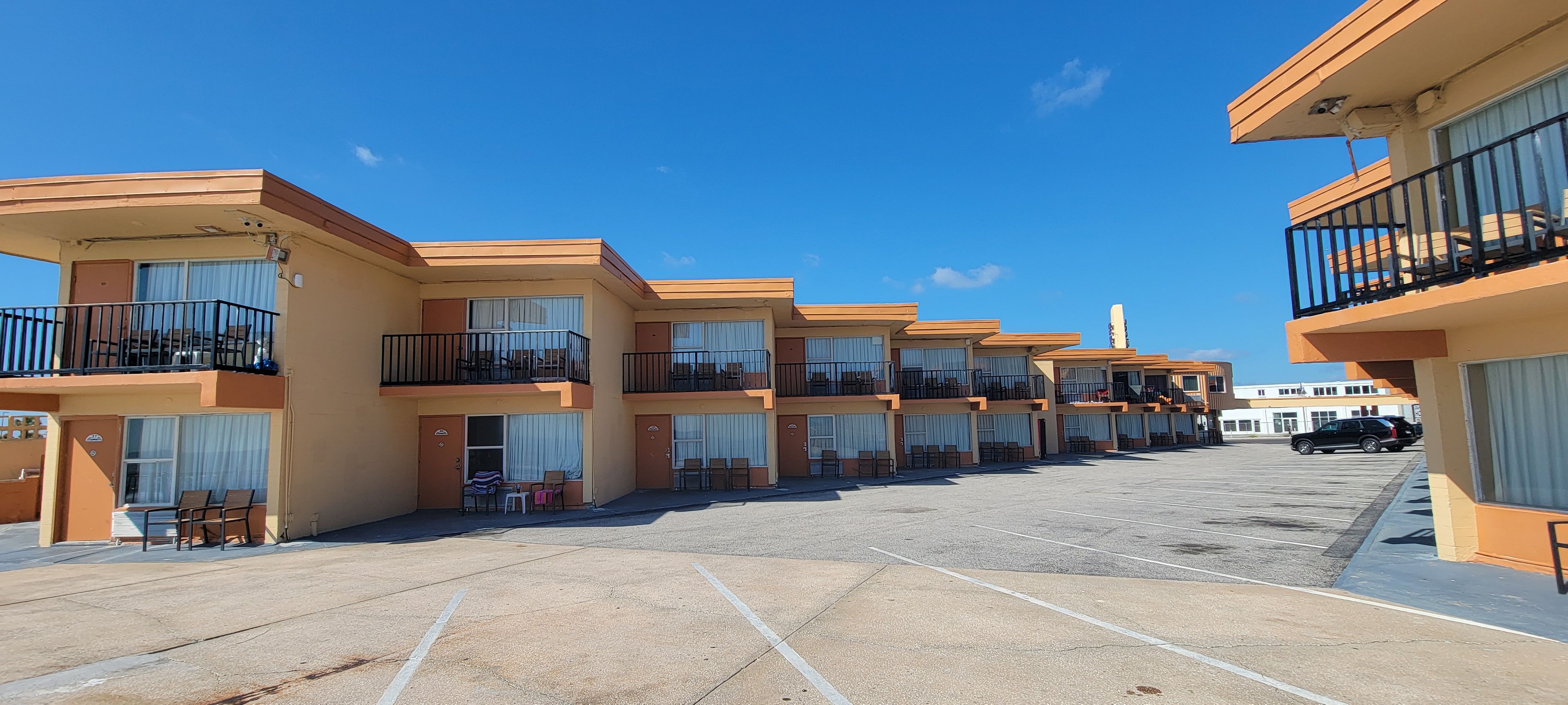 A row of hotel buildings with balconies, a parking lot, and a clear blue sky.