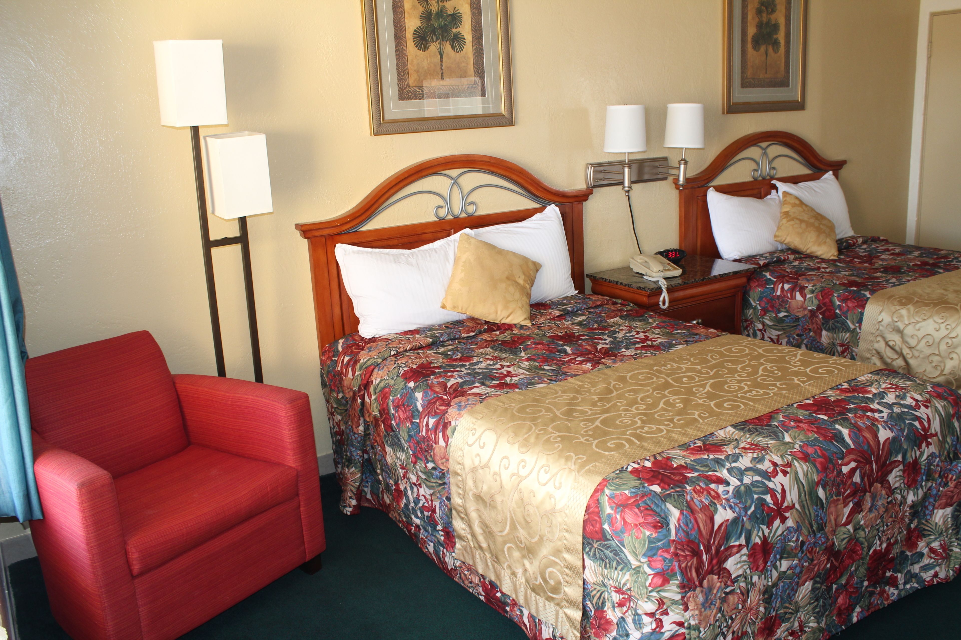 A hotel room with two beds, a red armchair, and a nightstand with a phone.