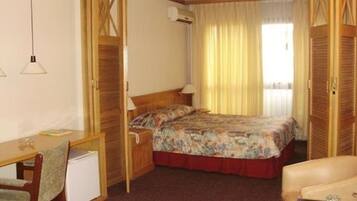 A hotel room with a bed, a desk, a chair, a small table, and a wardrobe.