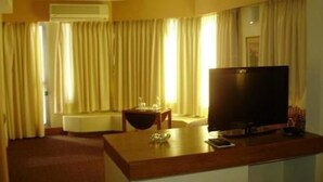 Quarto de hotel com uma televisão de tela plana grande, uma escrivaninha de madeira, uma mesa pequena e um sofá.