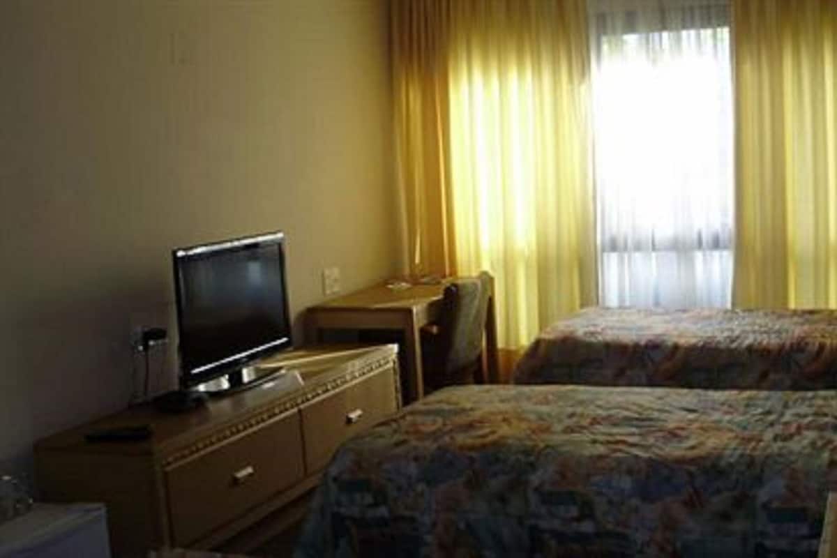 Quarto de hotel com duas camas, uma televisão sobre uma cômoda e uma janela com cortinas.
