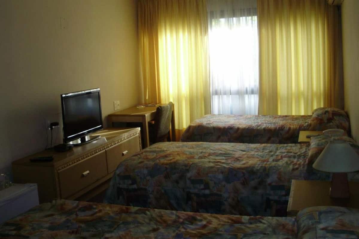 Quarto de hotel com duas camas, televisão, escrivaninha e janela com cortinas.