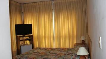 A hotel room with a bed, a television on a stand, a lamp, and curtains.