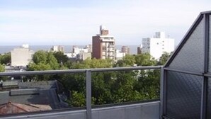 Varanda com guarda-corrimão de metal vista para uma paisagem urbana com edifícios e um corpo de água ao longe.