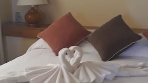 Uma cama com colcha branca e duas almofadas, uma vermelha e outra marrom.