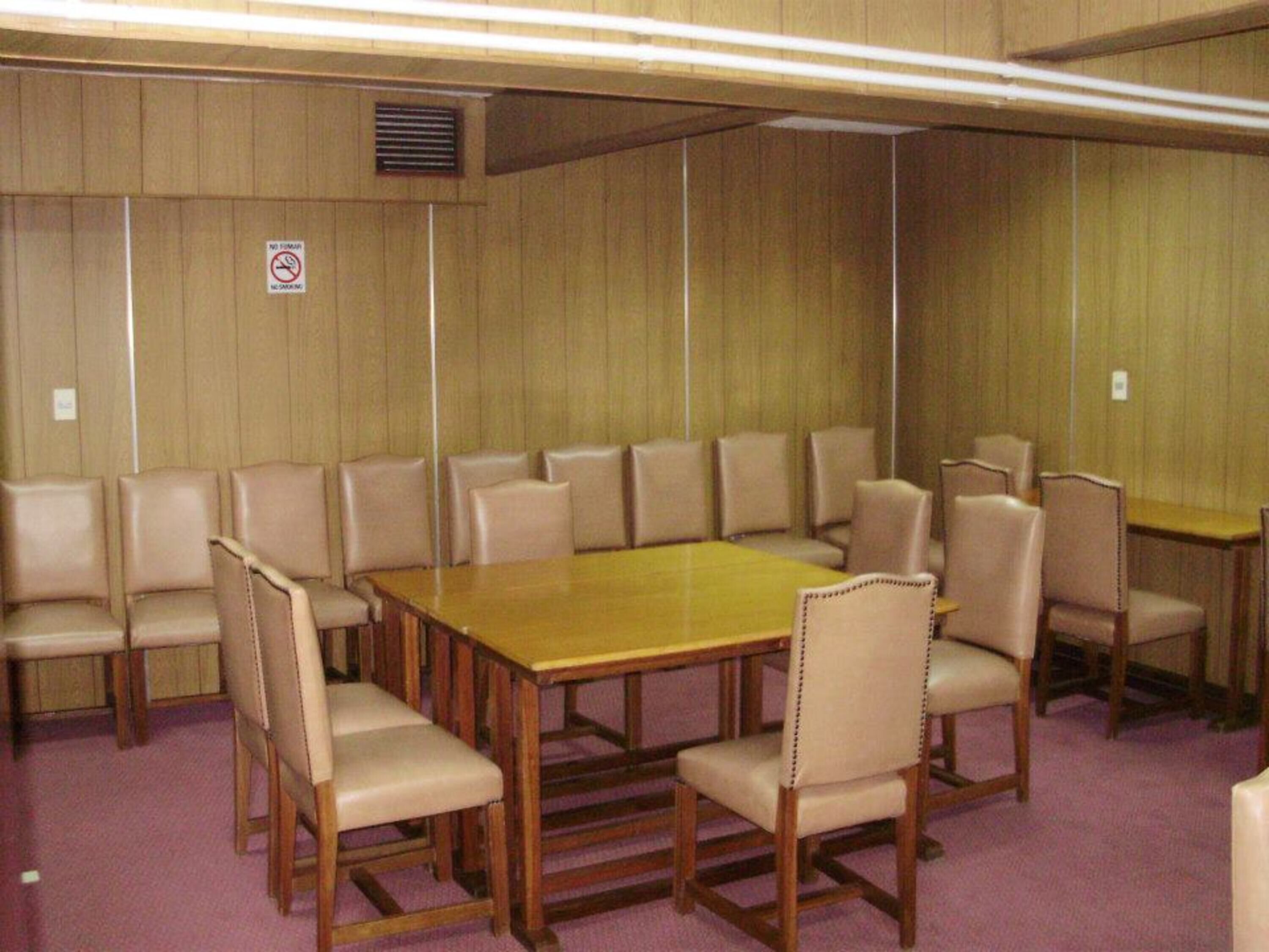 Un salón de conferencias con una gran mesa de madera rodeada de sillas color beige.
