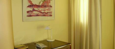 A hotel room with a desk, chair, lamp, and a painting on the wall.