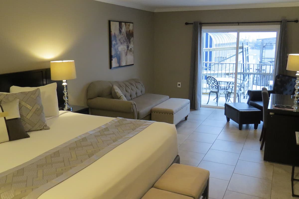 A hotel room with a large bed, a sofa, a desk, and a balcony with a view of the city.