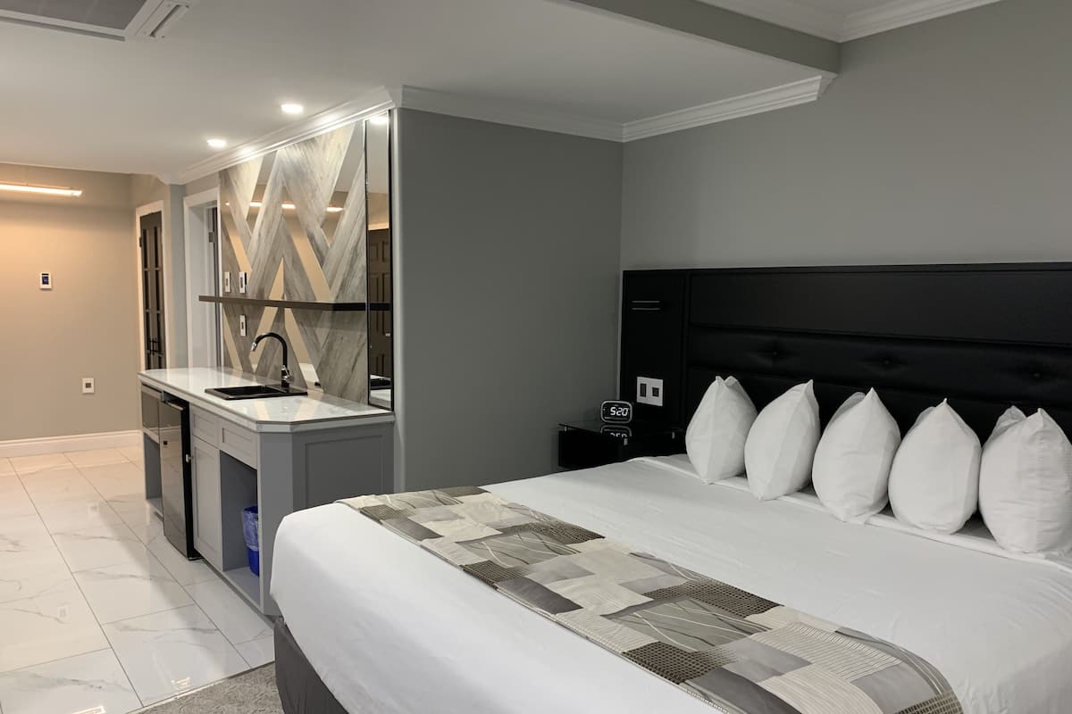 A modern bedroom with a large bed, a nightstand with a clock, and a bathroom with a vanity and mirror.