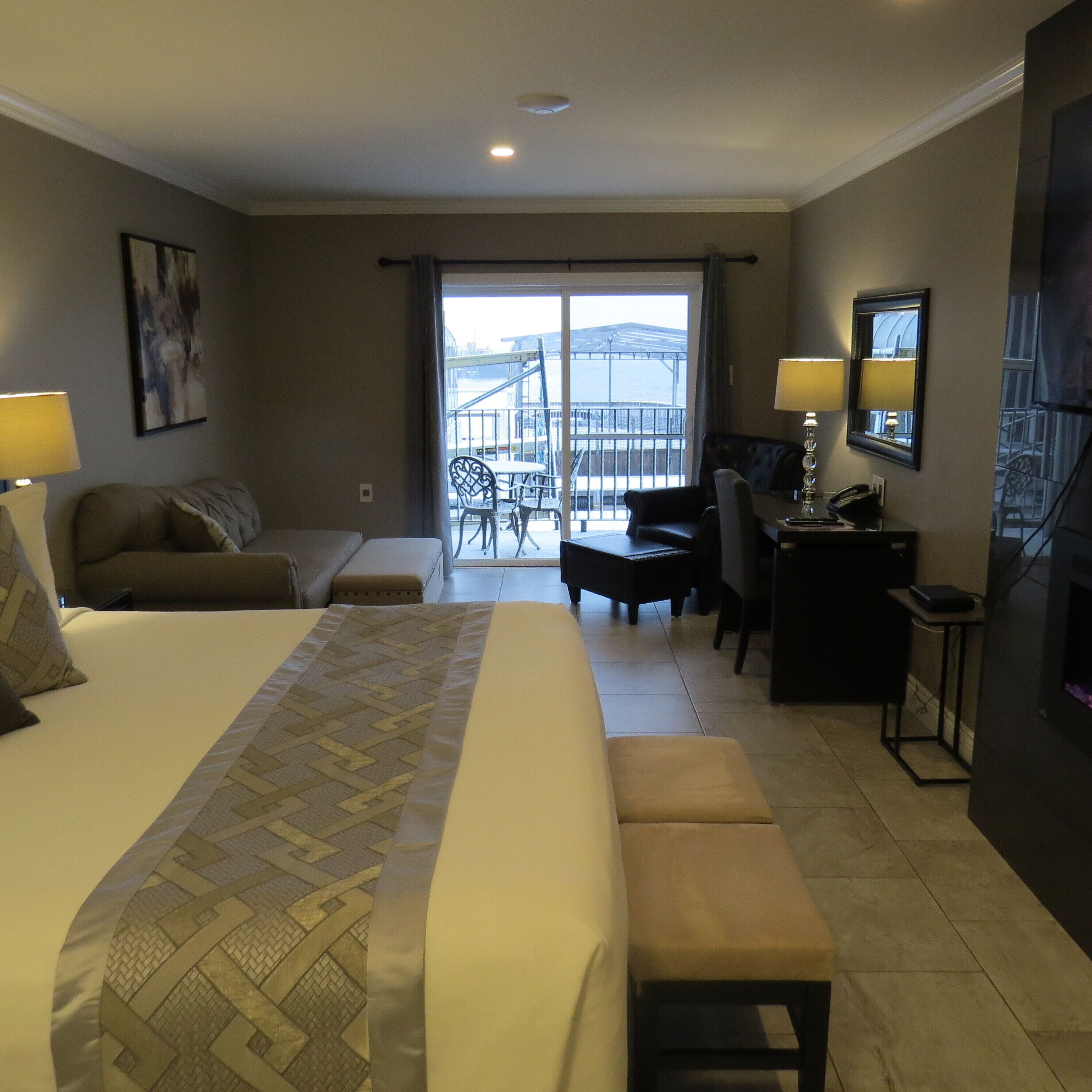 Habitación de hotel con una cama grande, un escritorio, una silla, un sofá y un balcón con vistas.