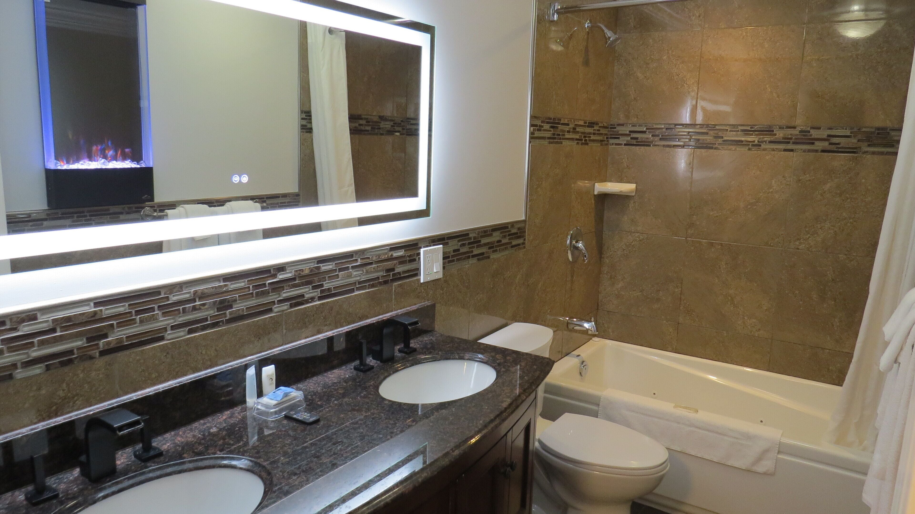 A bathroom with two sinks, a mirror, a shower, and a toilet.