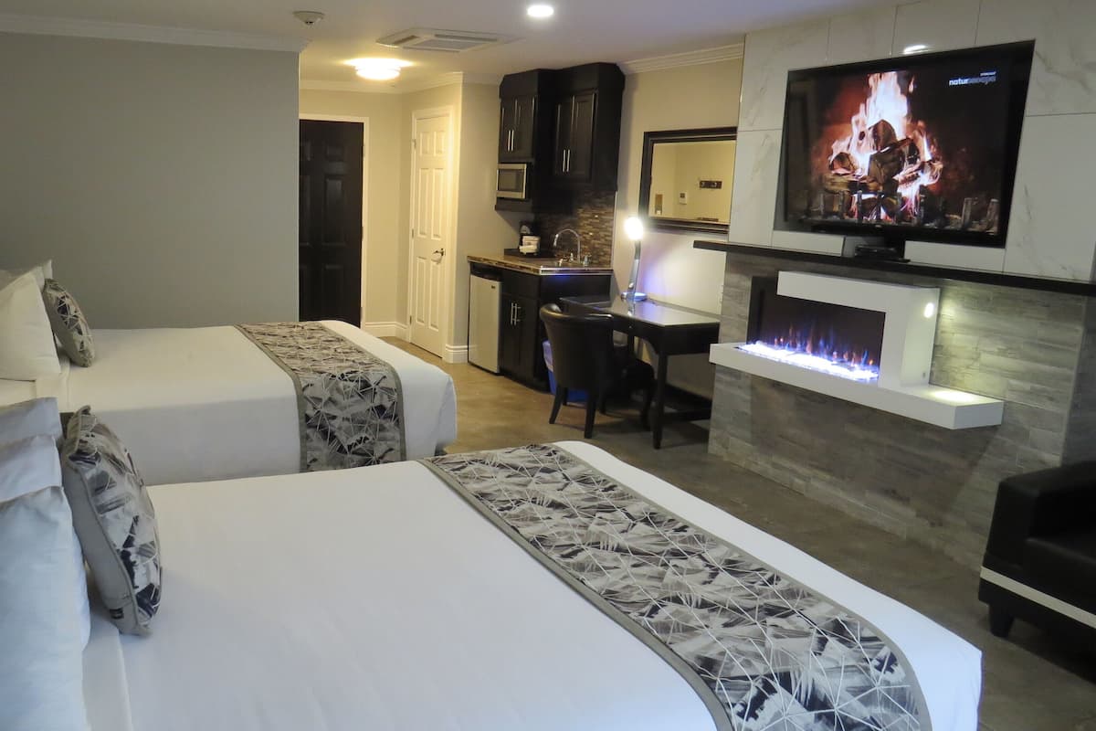 A hotel room with two beds, a desk, a television, and a fireplace.