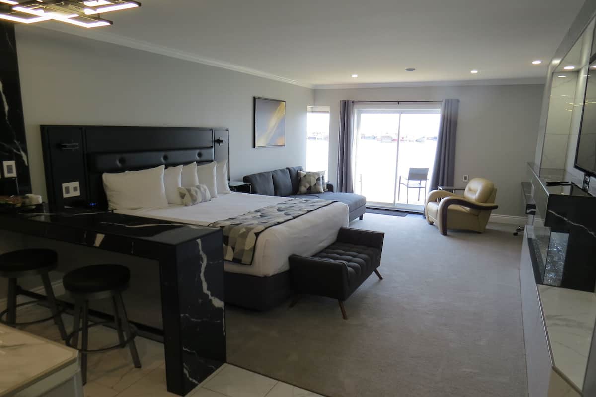 A modern hotel room with a large bed, a desk with bar stools, a sofa, and a television.