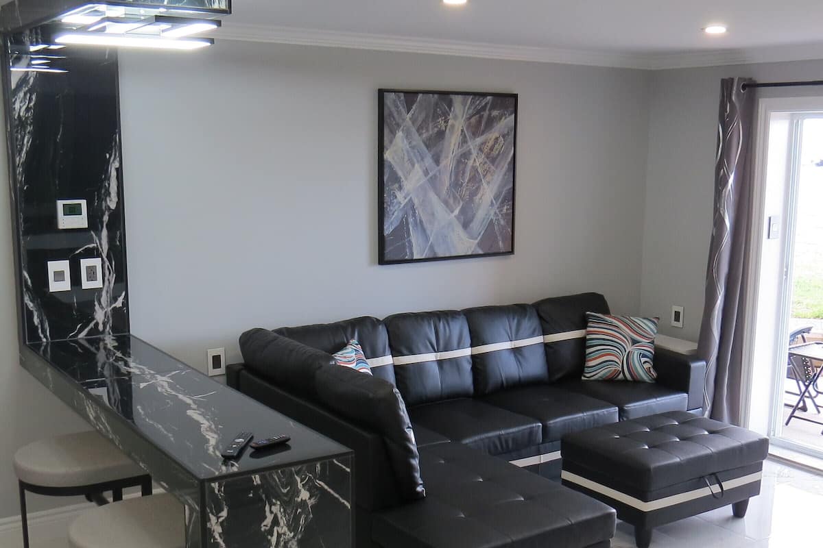 A modern living room with a black leather sofa, a marble bar, and a large abstract painting on the wall.