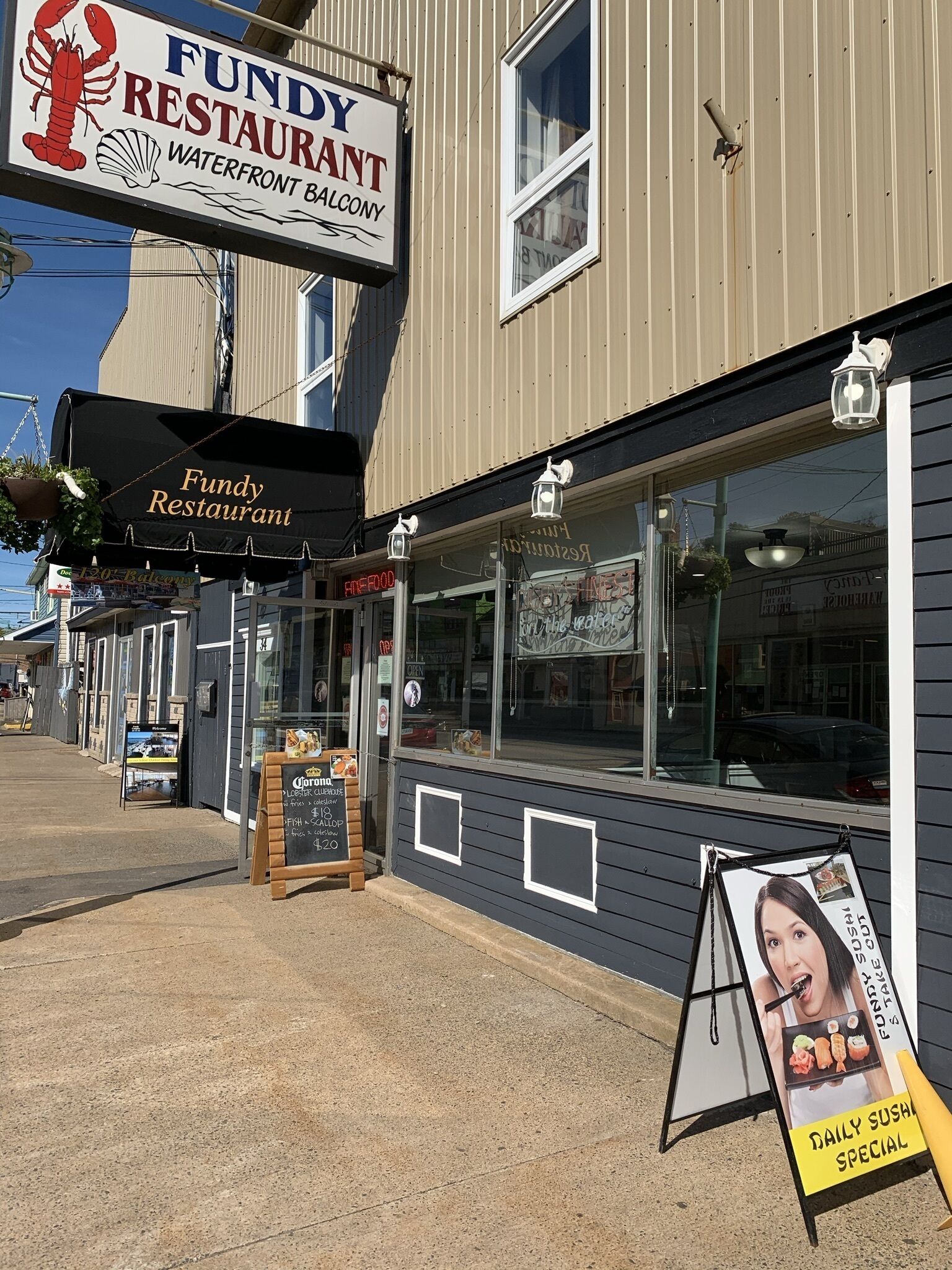 A waterfront restaurant named 'Fundy Restaurant' with a sign featuring a lobster and a scallop.
