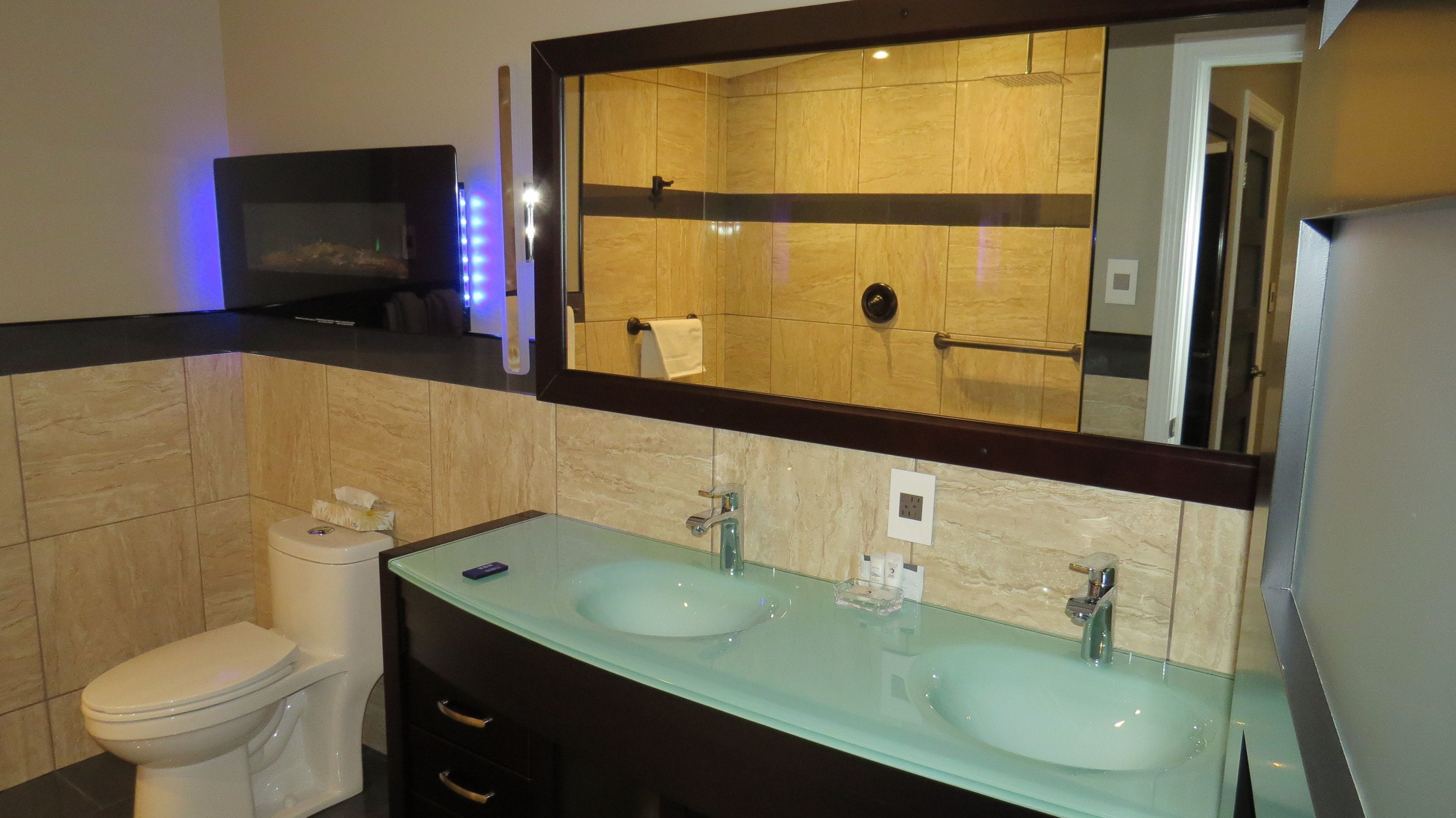 Een moderne badkamer met twee glazen wastafels, een toilet en een grote spiegel.