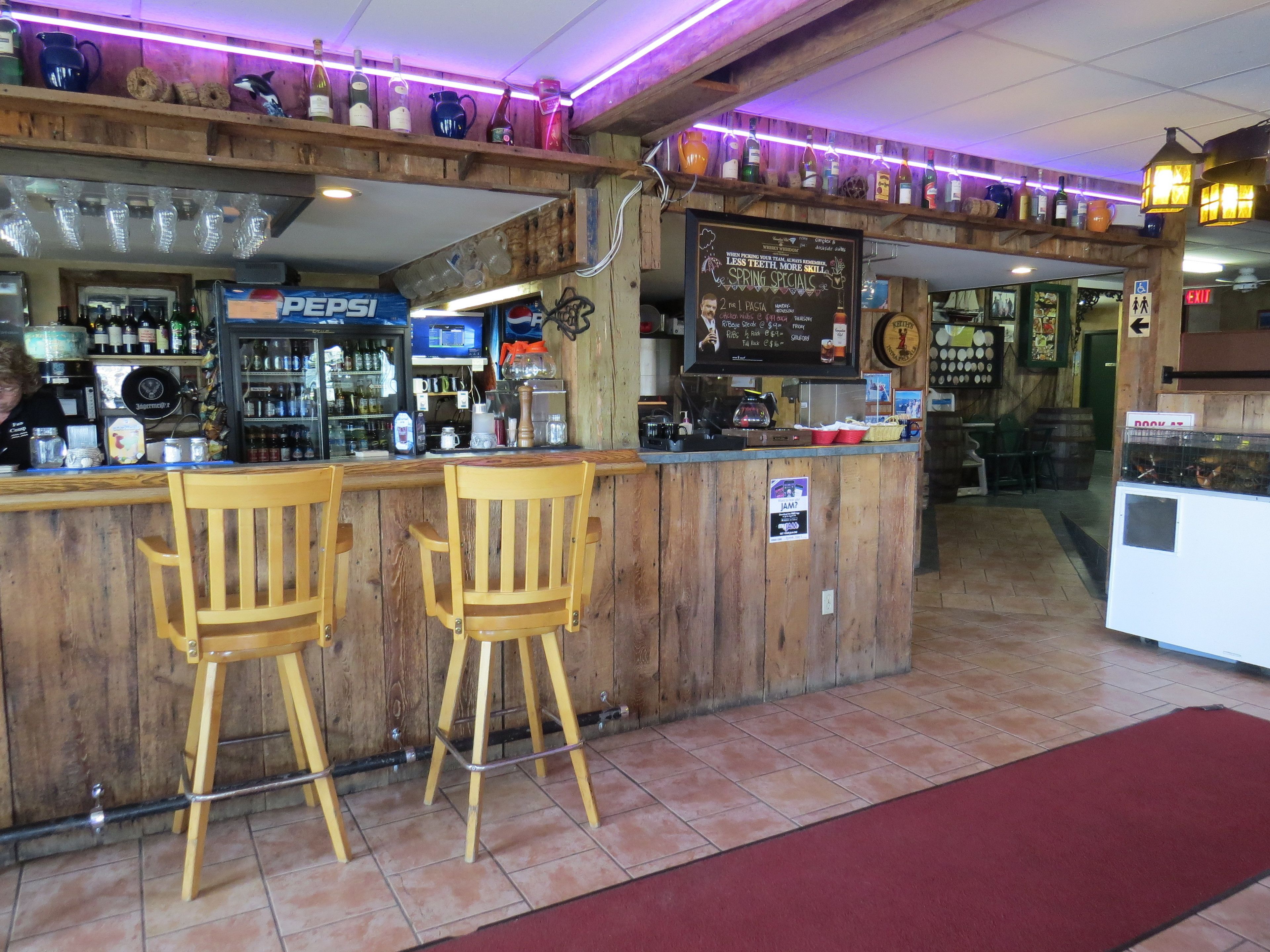 Zona de bar con taburetes de madera, una barra con diferentes botellas y un panel con la carta.