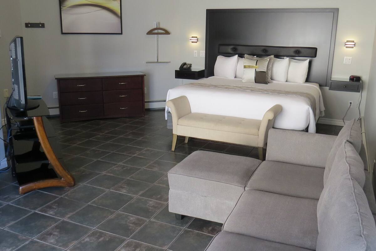 A modern hotel room with a large bed, a sofa, a TV, and a desk.