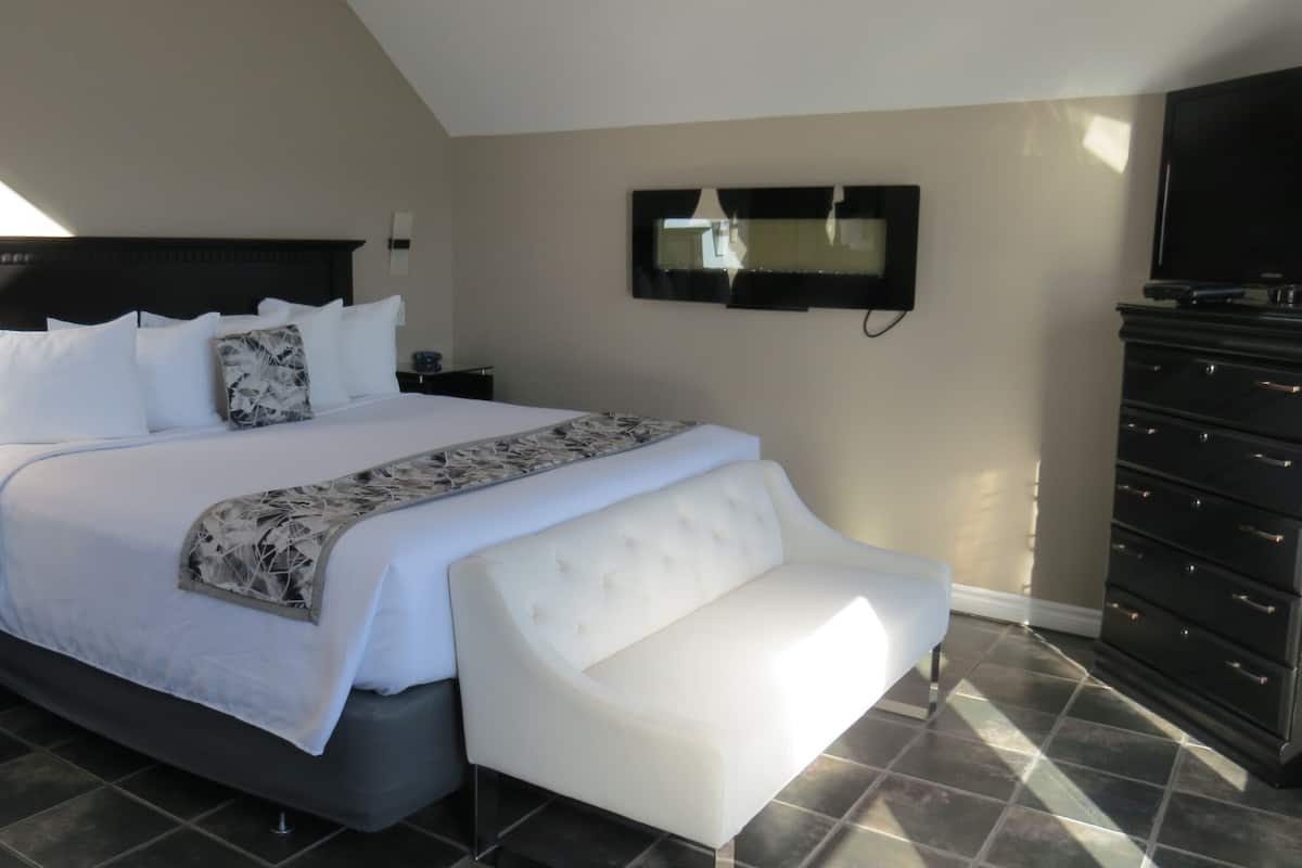 A modern bedroom with a large bed, a flat-screen TV, a dresser, and a bench.