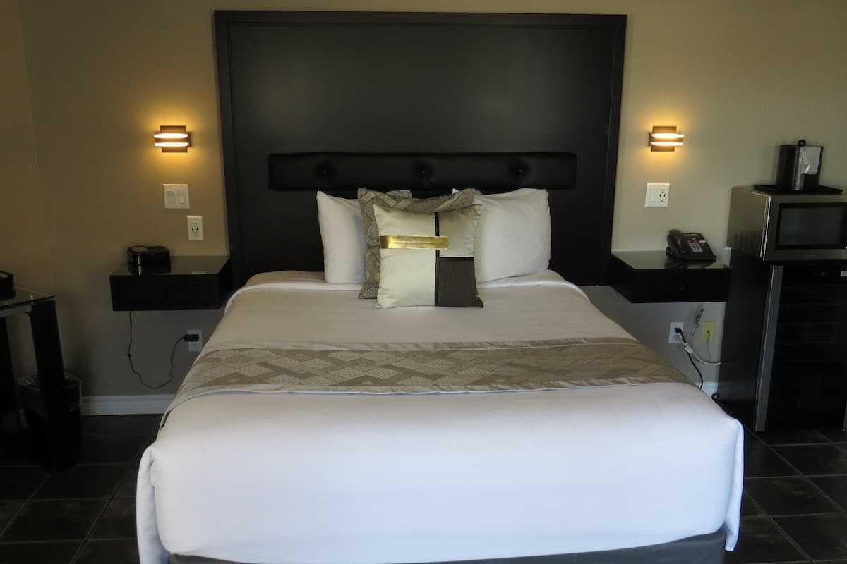 A large bed with a dark headboard, two bedside tables with lamps, and a microwave on the right side.