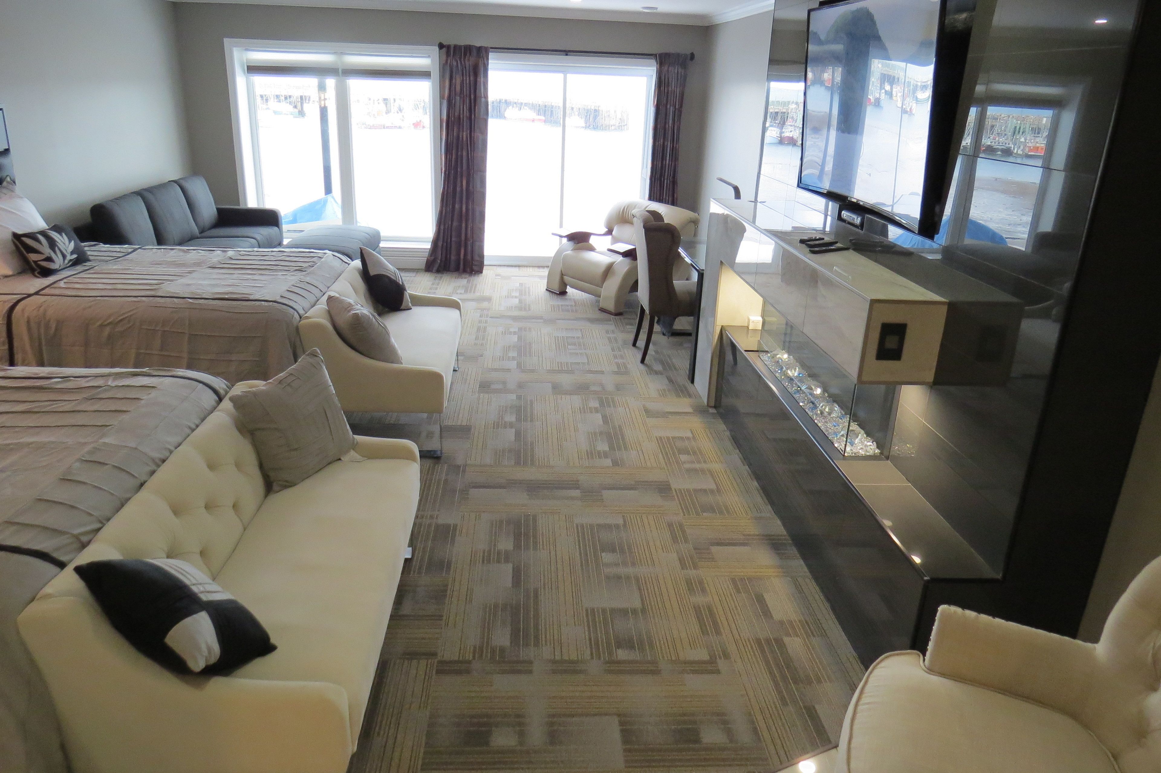 Habitación de hotel con una cama grande, un sofá, un escritorio con televisor y vistas al exterior a través de las ventanas.