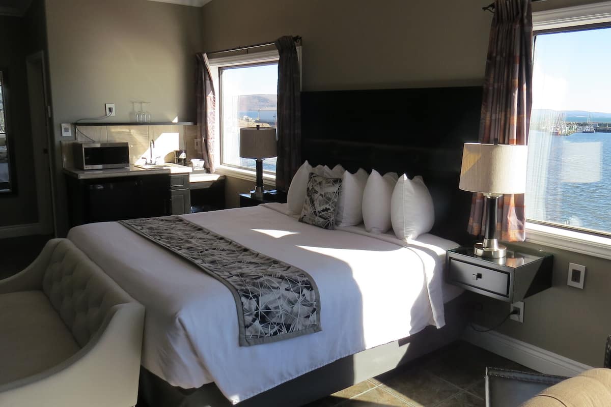 A hotel room with a bed, a desk, a chair, a TV, and a view of the sea.