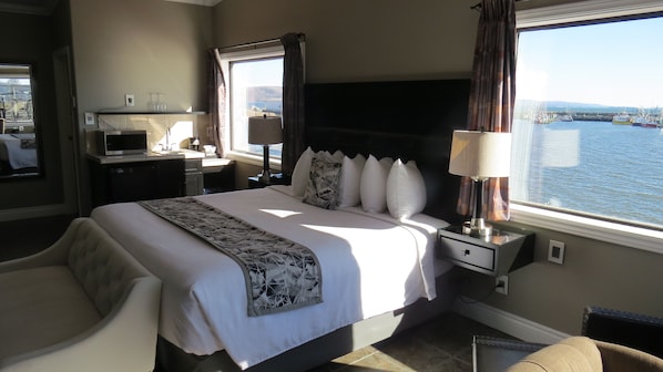 A hotel room with a bed, a desk, a chair, a TV, and a view of the sea.