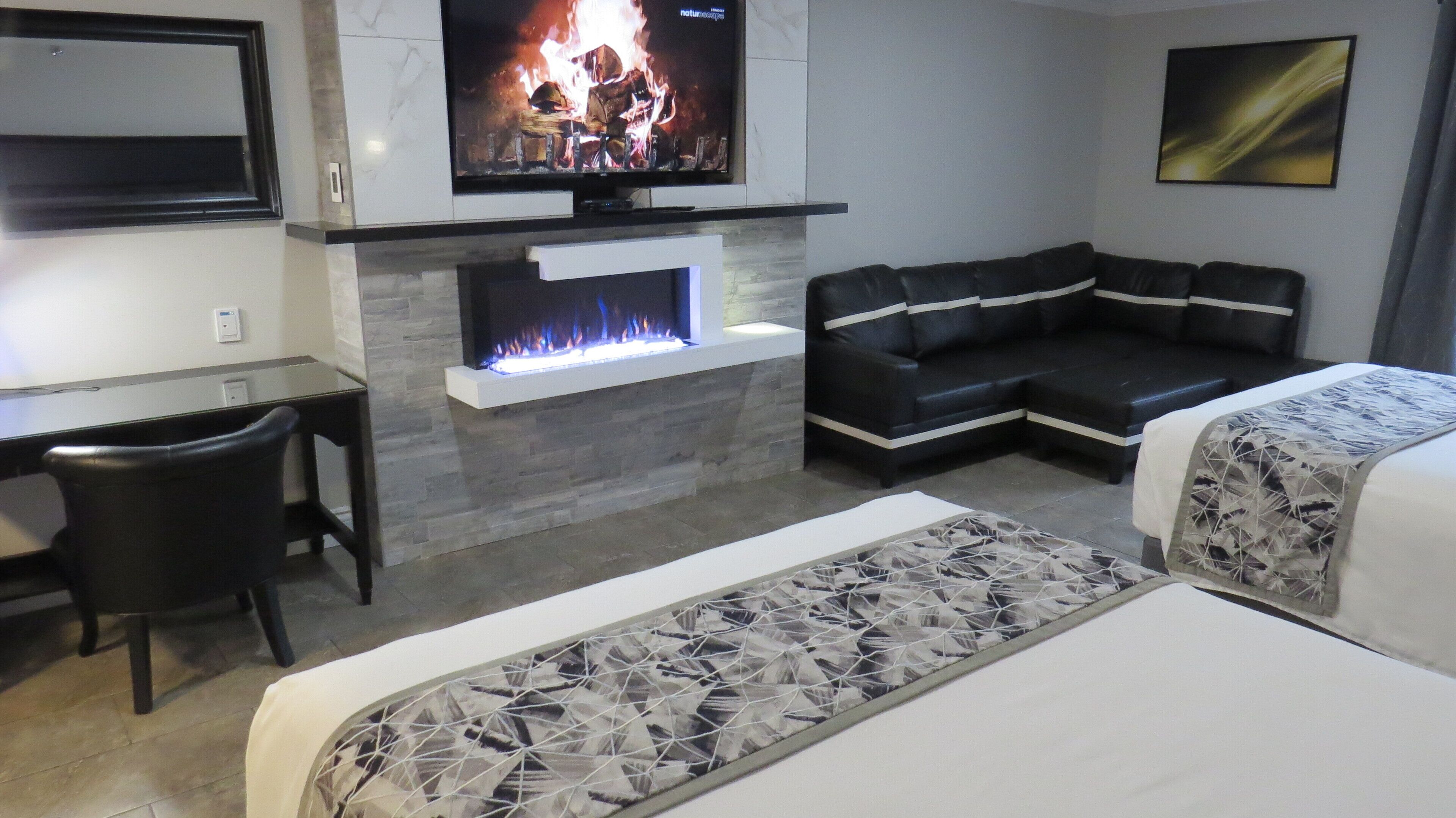 A hotel room with a fireplace, a sofa, a desk, and a bed.